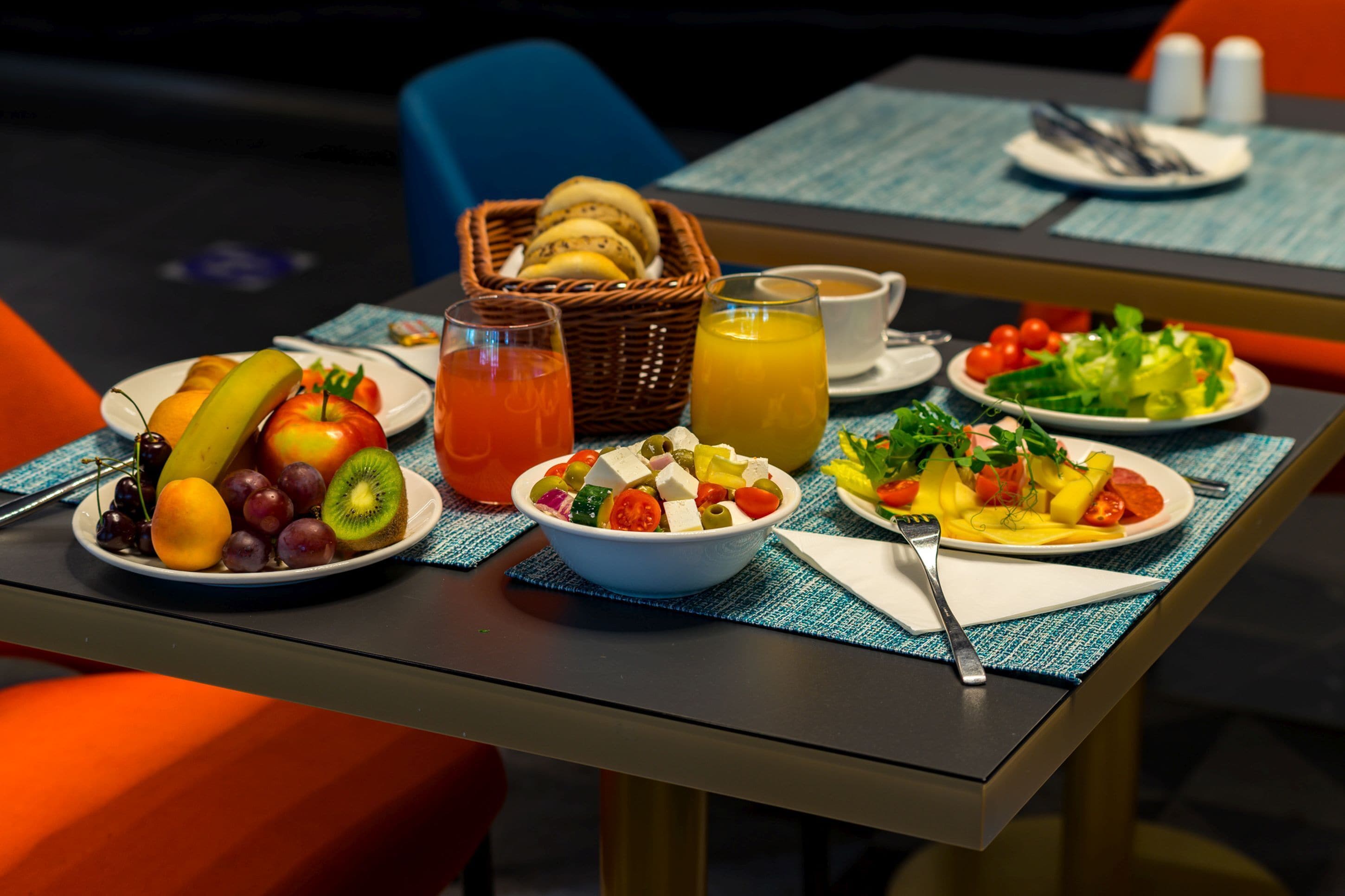 Una mesa de desayuno con diversas frutas, un tazón de ensalada y una cesta de pan.