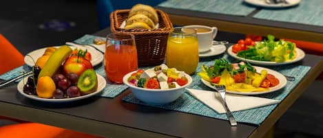 A breakfast table with various fruits, a bowl of salad, and a basket of bread.