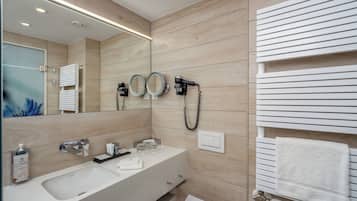 Un baño moderno con un espejo grande, dos secadores de pelo, un perchero para toallas y un lavamanos con dispensador de jabón.