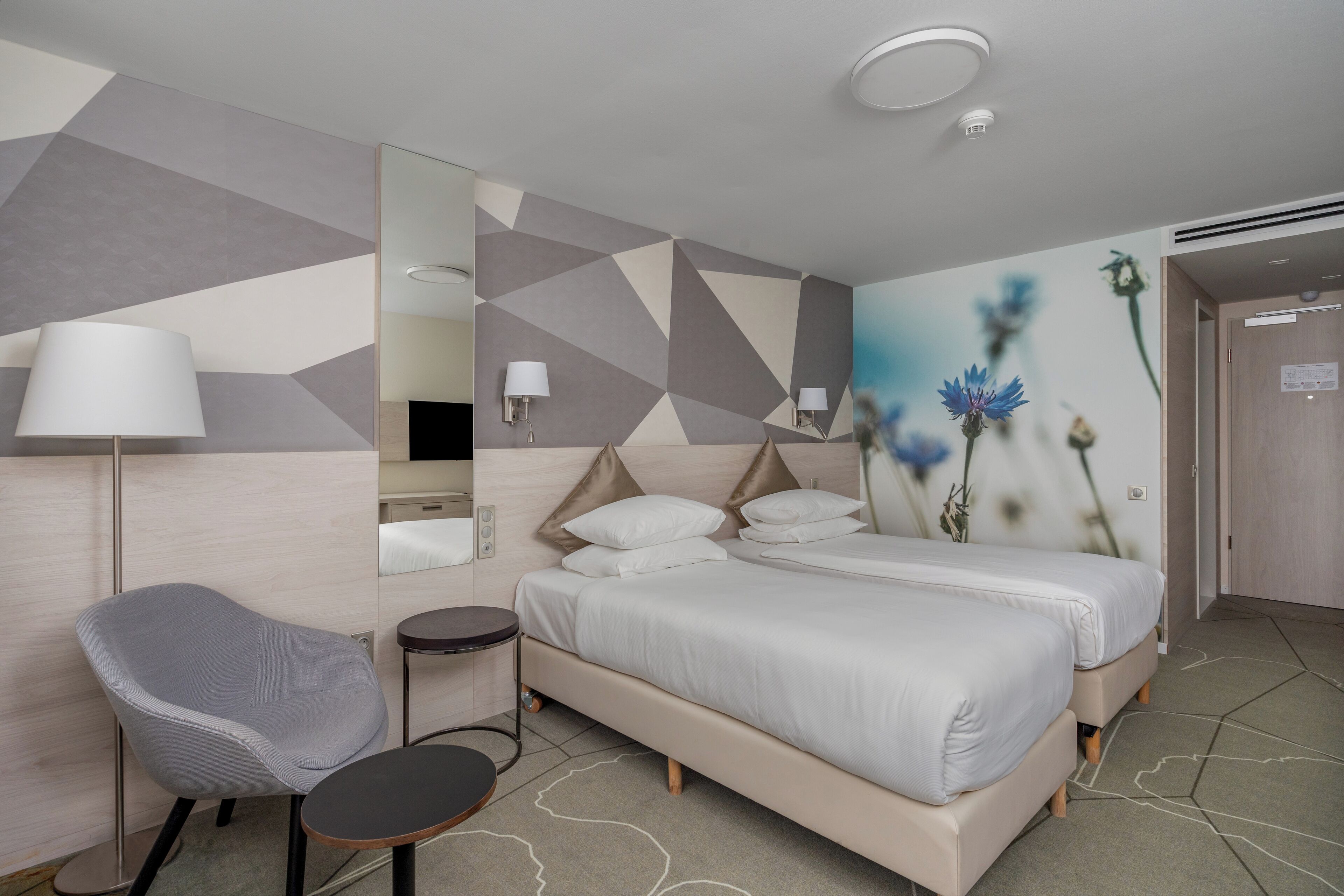 A modern hotel room with a large bed, a chair, a small table, and a mirror.