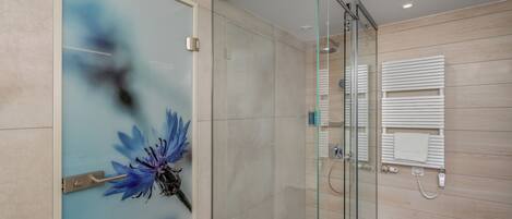 Un baño moderno con cabina de ducha de vidrio, suelo de madera y un diseño floral azul decorativo en la puerta.