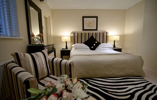 Ein Hotelzimmer mit einem Bett, zwei Nachttischen mit Lampen, einem Sessel, einem Teppich mit ZEBRA-MUSTER und einem Spiegel an der Wand.