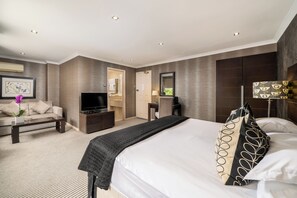A modern hotel room with a large bed, a flat-screen TV, a sofa, a desk, and a mirror. - The Beaufort Knightsbridge (London)