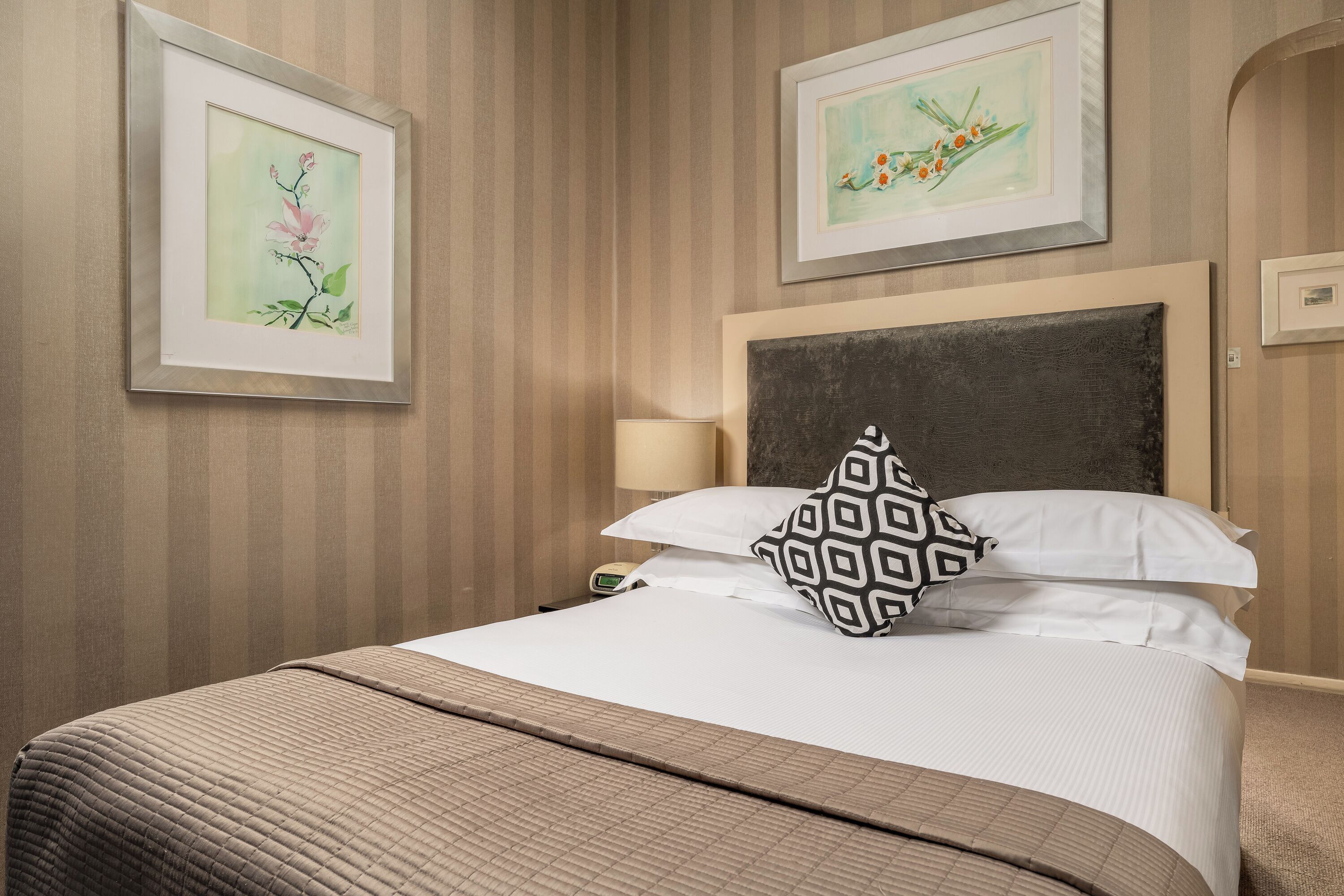 A neatly made bed with a patterned pillow, a bedside lamp, and two framed artworks on the wall.