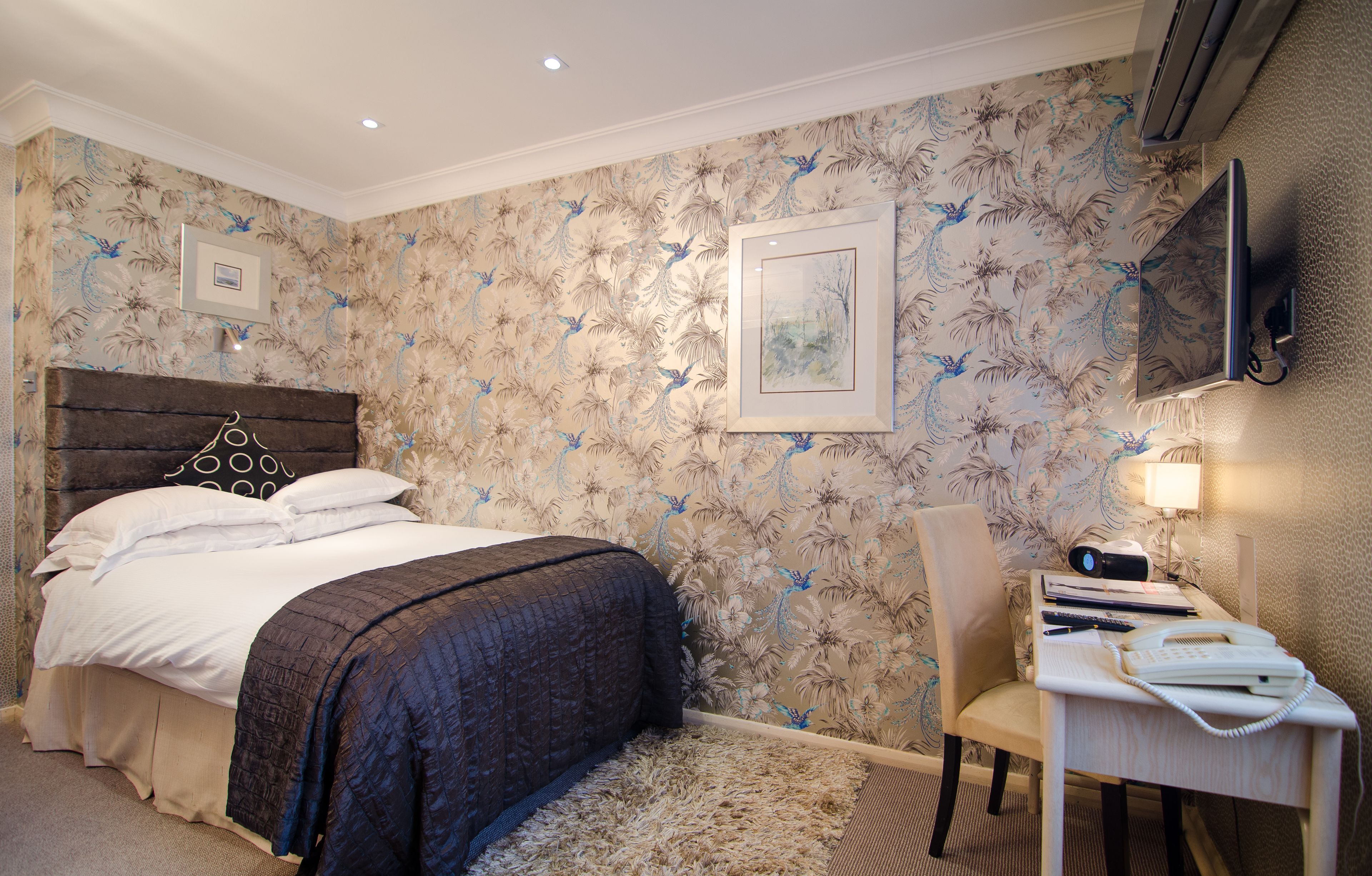 A bedroom with a bed, a desk with a telephone, and a chair.