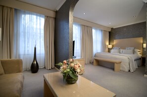 A hotel room with a bed, a sofa, a desk, and a vase of flowers. - The Beaufort Knightsbridge (London)