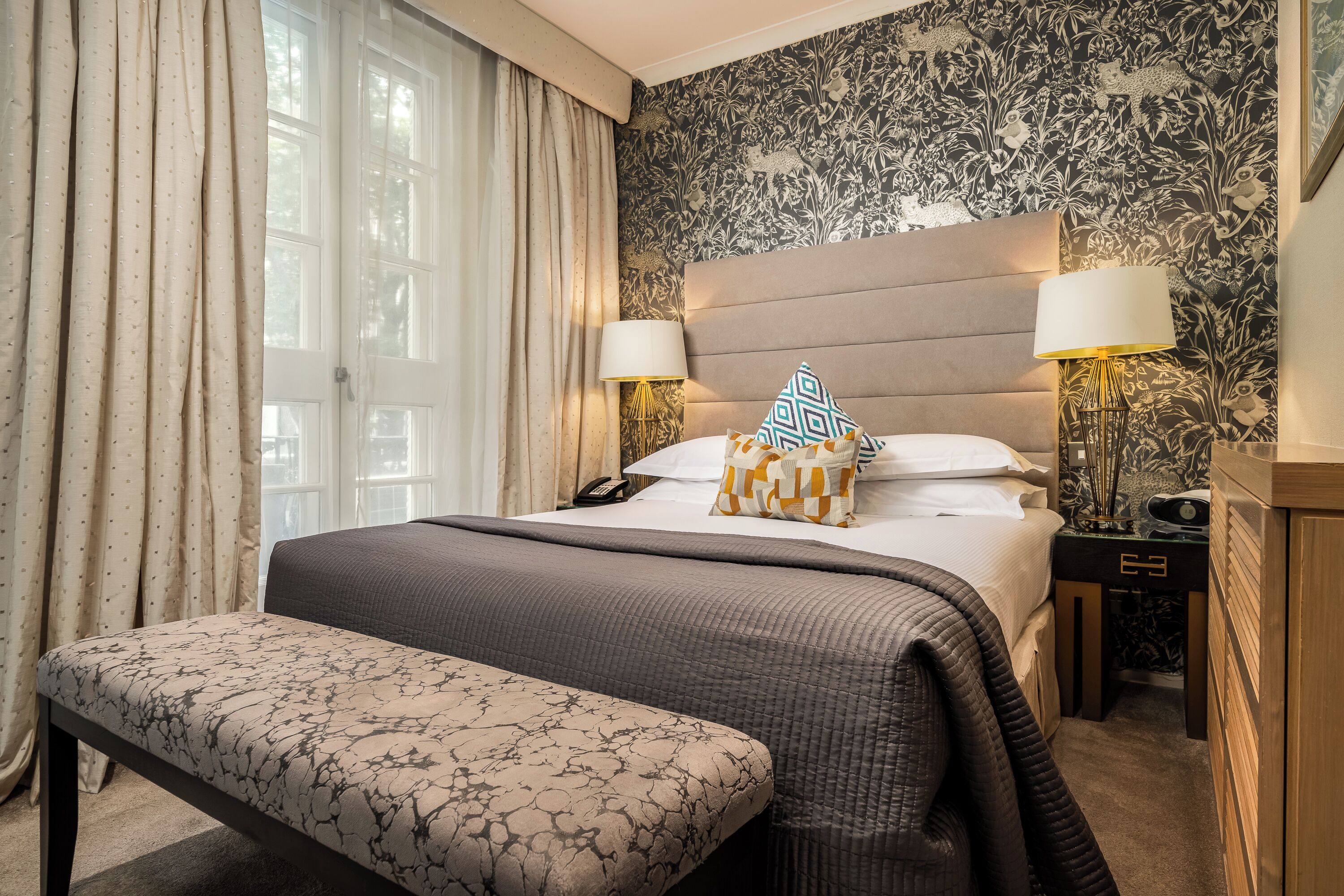 Una camera d'albergo con un letto grande, abat-jour, una panca e carta da parati decorata.