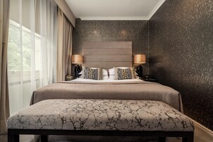 A neatly made bed with a headboard, two bedside lamps, and a patterned bench in front.