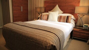 Ein Hotelzimmer mit einem großen Bett, einem Holzkopfende, zwei Nachttischen mit Lampen und einem Beistelltisch mit einer Uhr.