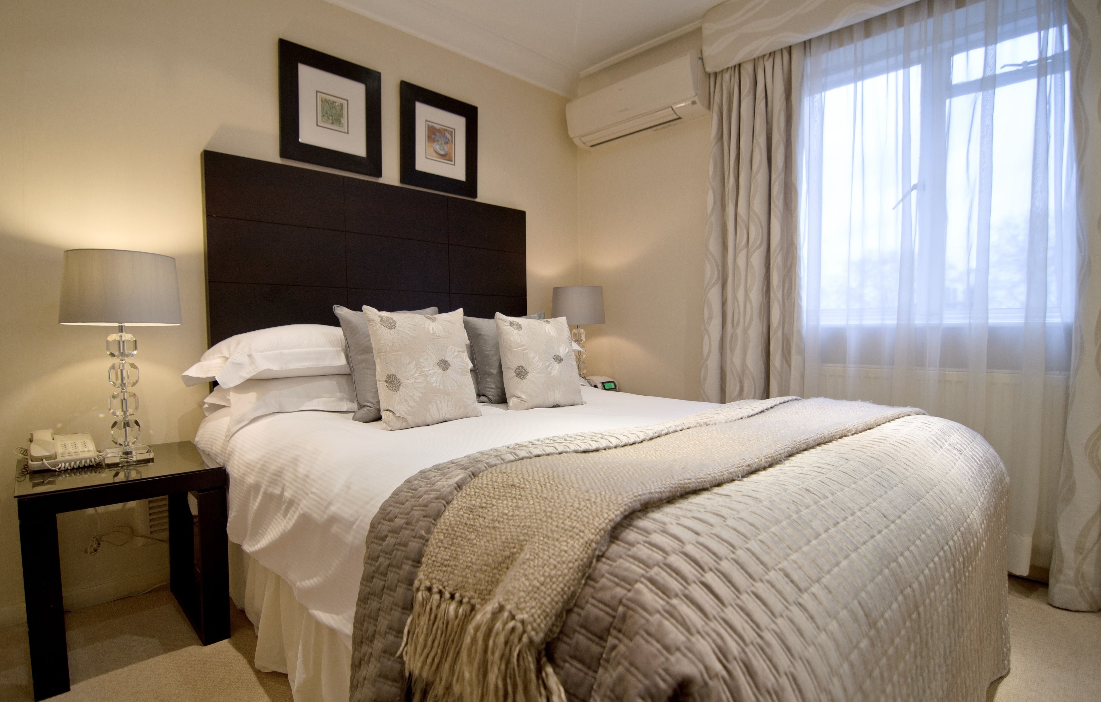 A neatly made bed with a dark headboard, two bedside lamps, and a telephone on a small table beside it.