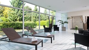A modern indoor area with large windows, sun loungers, and a small table with a plant. - Leonardo Hotel Monchengladbach (Moenchengladbach)