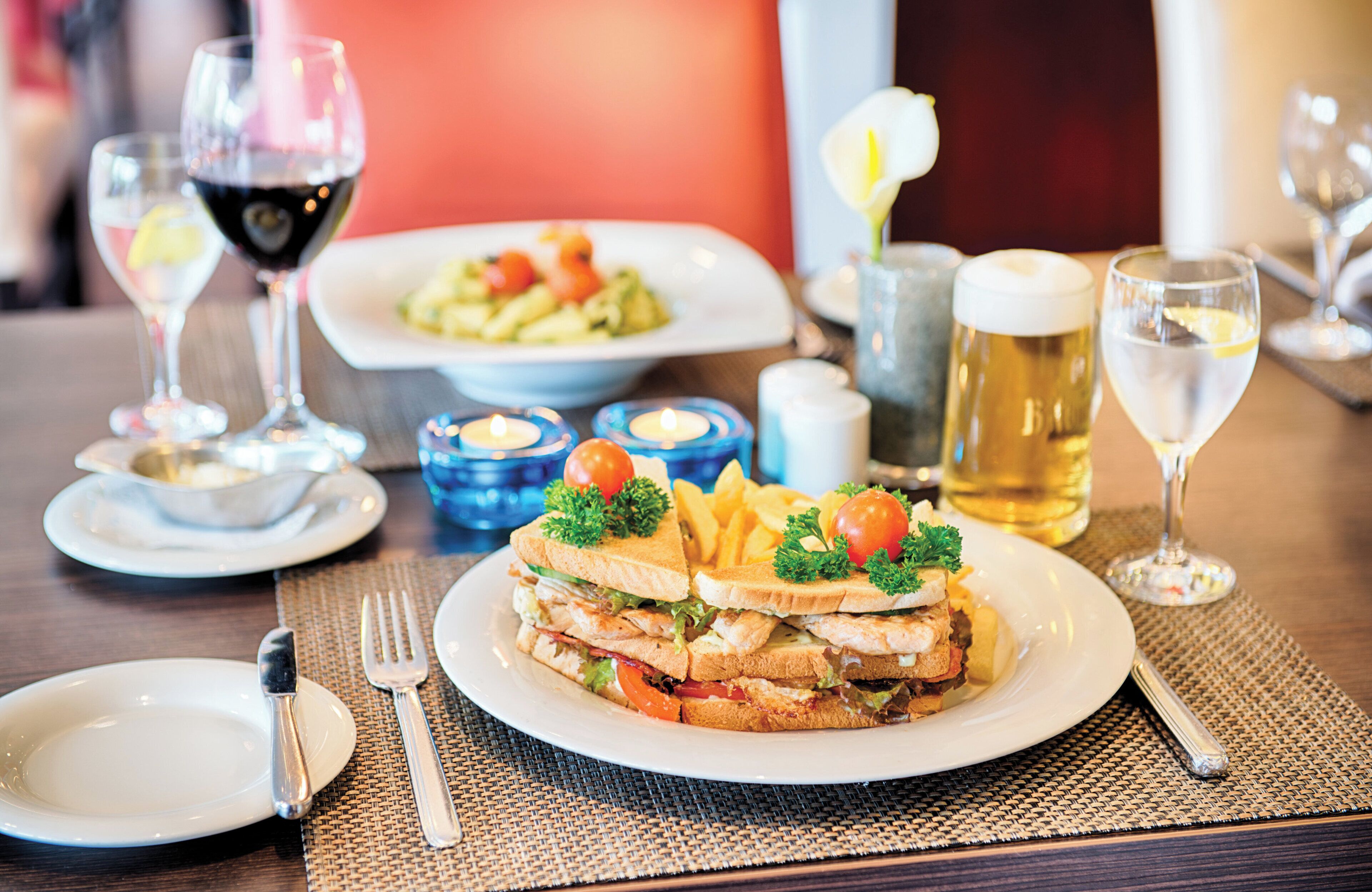 A dining table with a sandwich, fries, and a plate of salad. There are also glasses of wine and a beer mug.
