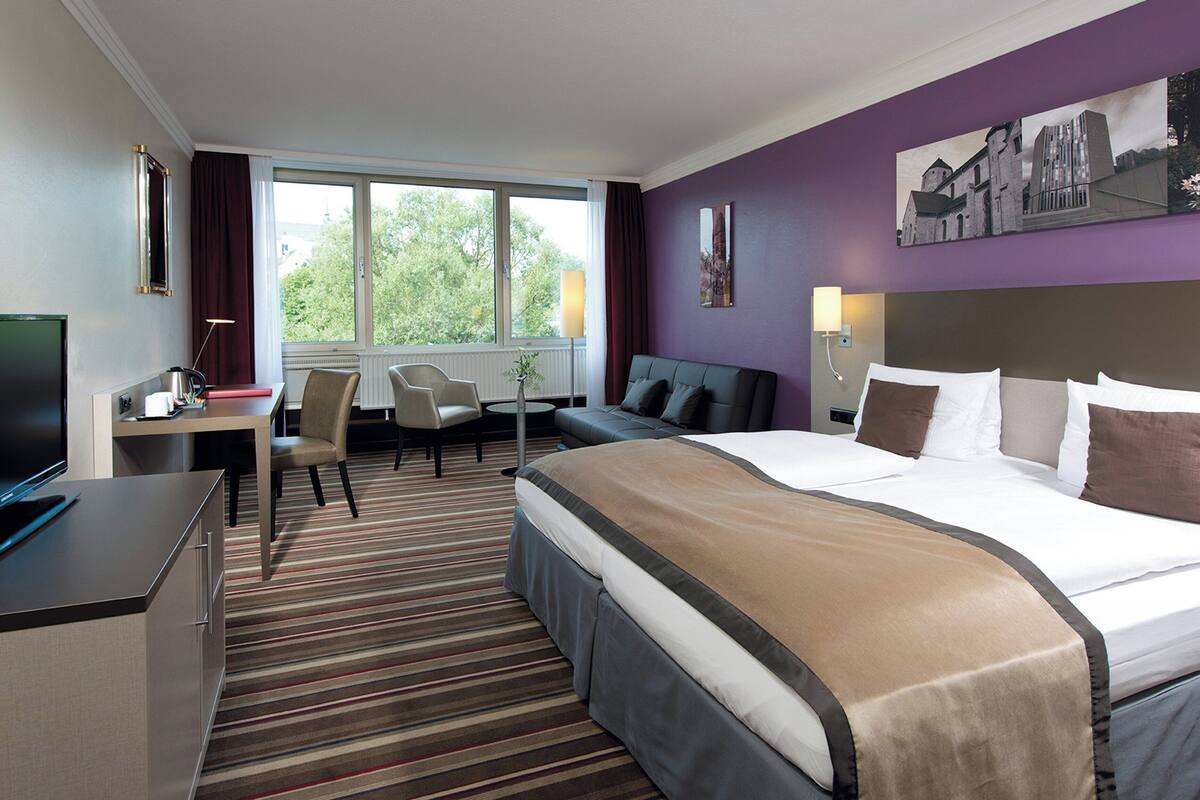 Una habitación de hotel con una cama grande, un escritorio con ordenador, una silla y un televisor.