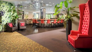 A hotel lobby with a bar area, seating, and large plants. - Leonardo Hotel Monchengladbach (Moenchengladbach)