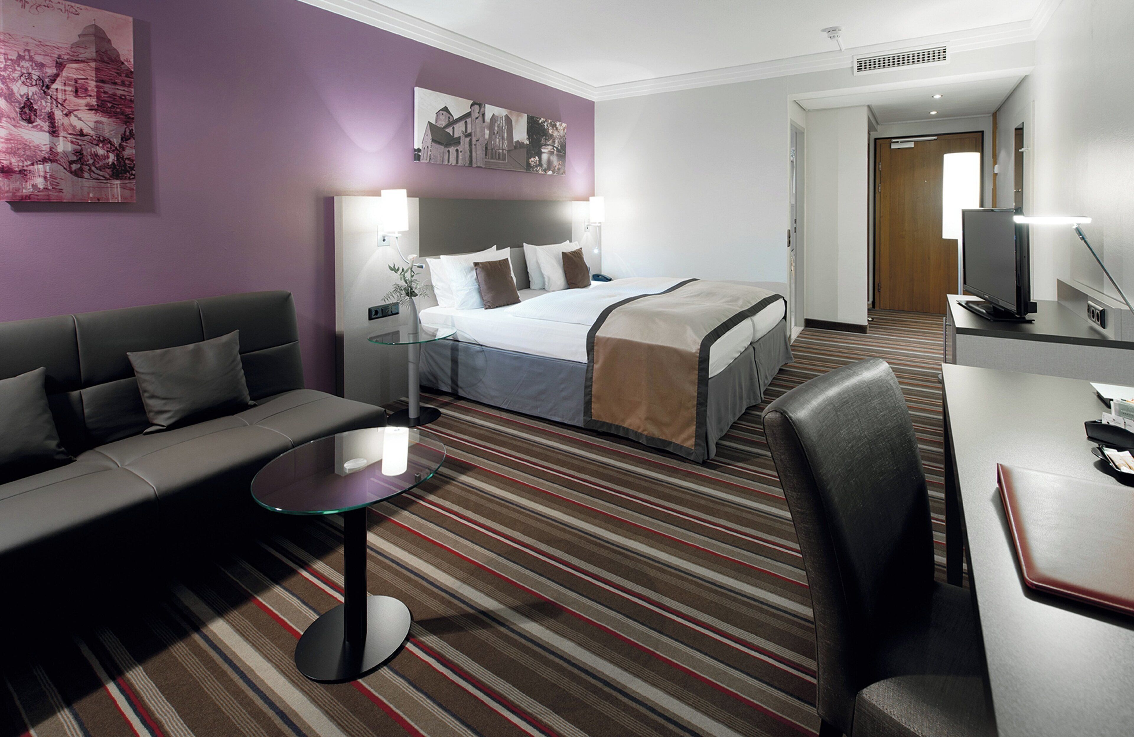 A hotel room with a bed, a sofa, a desk, and a television.