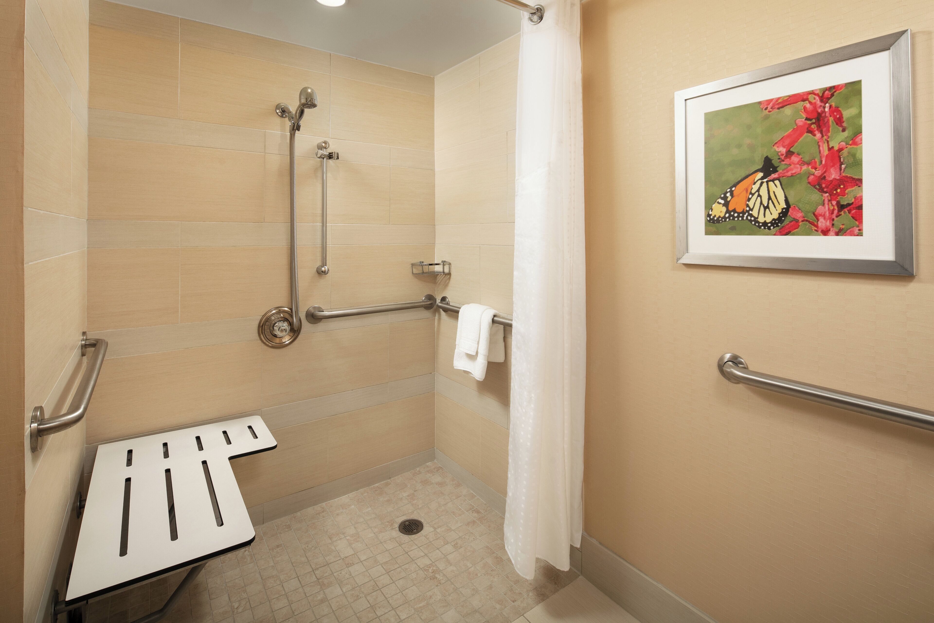 A shower with grab bars, a white towel, and a framed picture on the wall.