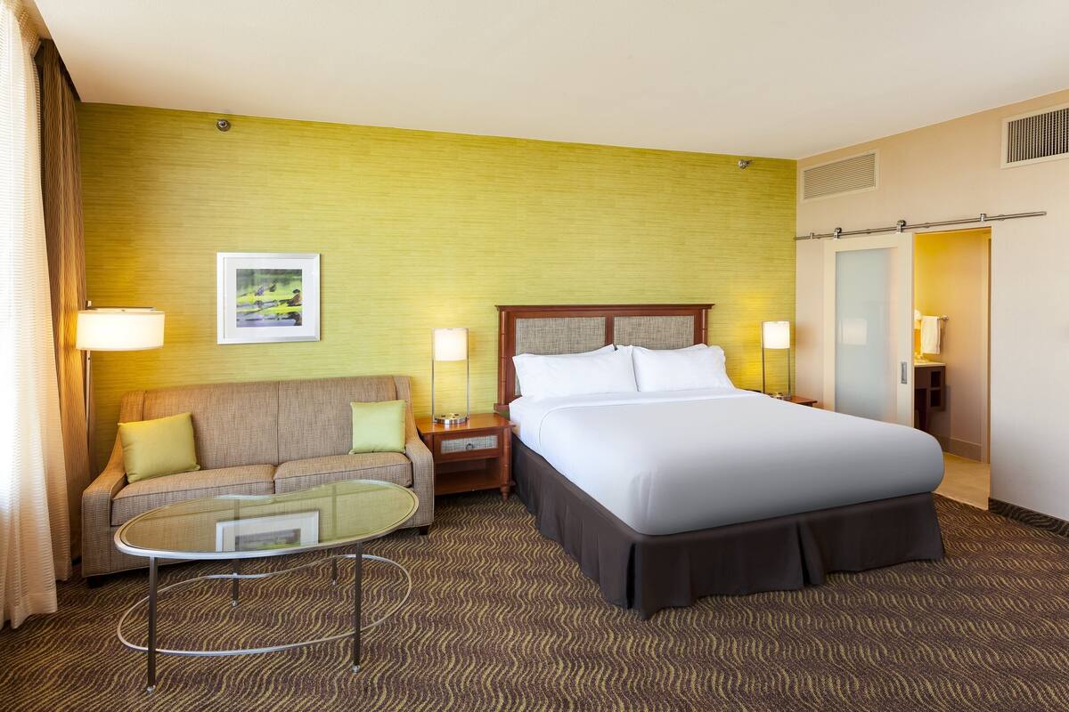 A hotel room with a bed, a sofa, a small table, and a picture on the wall.