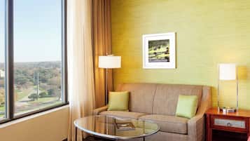 Habitación de hotel con vistas a un paisaje urbano, un sofá con cojines, una mesita de vidrio y una lámpara.