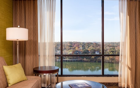 A hotel room with a large window offering a view of a lake and autumn foliage.