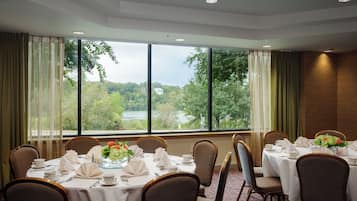 A conference room with tables set for a meeting, large windows with a view of trees and a lake, and a carpeted floor.