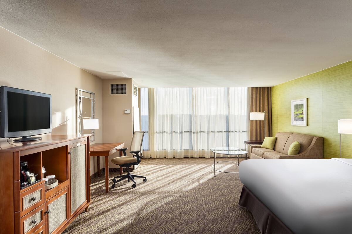 A hotel room with a large bed, a desk with a chair, a television, and a sofa.