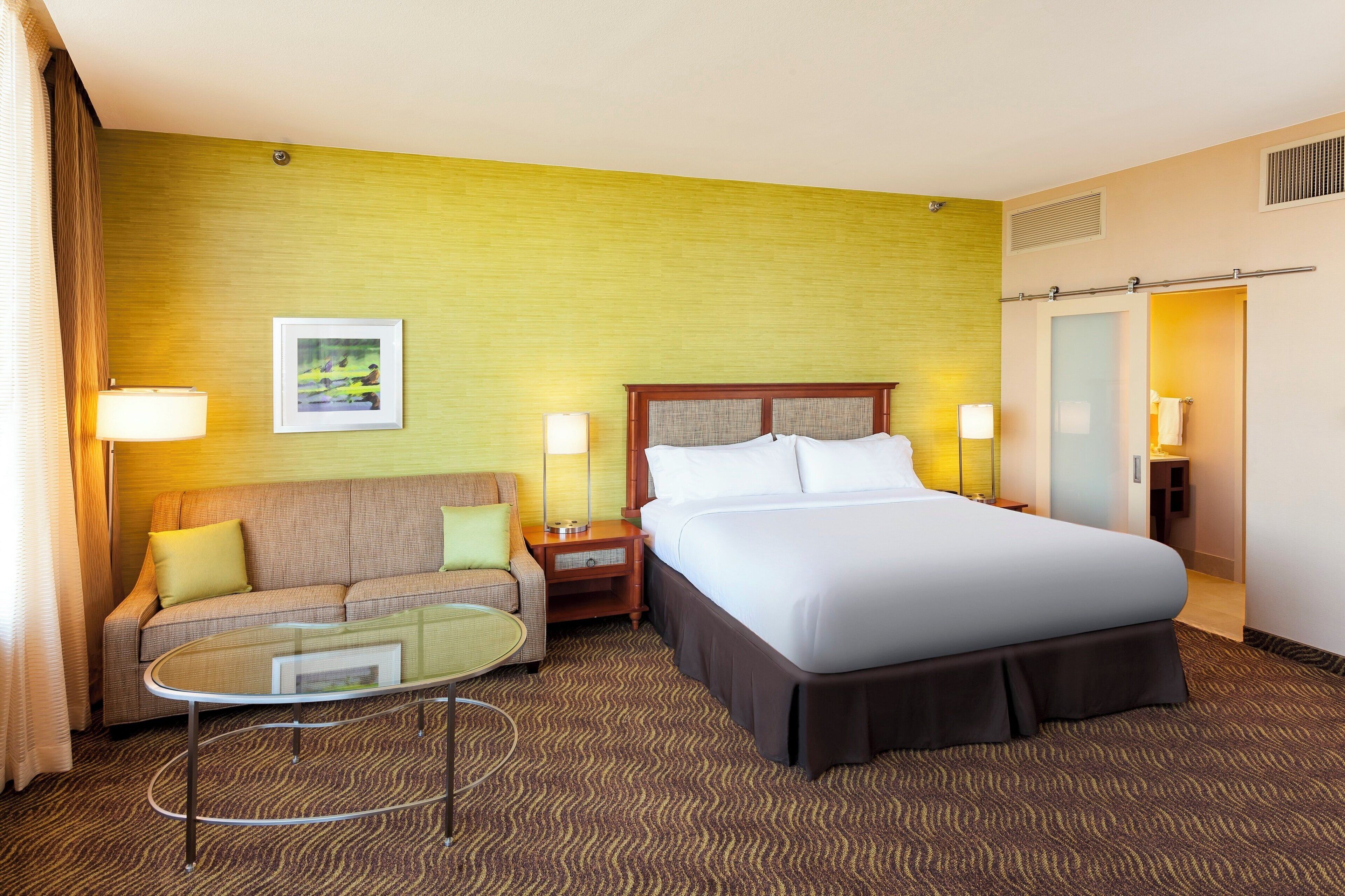 A hotel room with a bed, a sofa, a small table, and a picture on the wall.