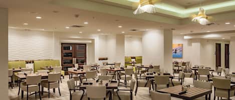 A spacious dining area with multiple tables and chairs, recessed lighting, and a modern ceiling design.