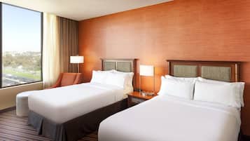 A hotel room with two beds, a large window with a view, a wooden wall, and a nightstand with a lamp.