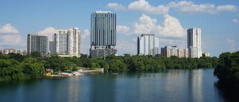 A cityscape with high-rise buildings along a river, surrounded by greenery.