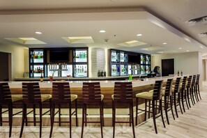 Zona de bar com várias opções de assento e uma variedade de garrafas nas prateleiras.