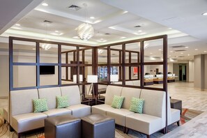 A hotel lobby with a seating area, a reception desk, and a modern chandelier.