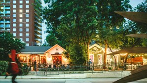 A restaurant with outdoor seating, a building in the background, and a pedestrian crossing the street.