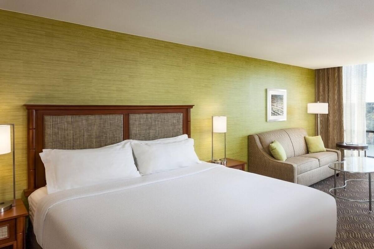 A hotel room with a large bed, a sofa, a small table, and a lamp.