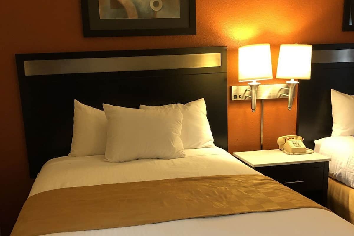 A hotel room with a large bed, two bedside lamps, a telephone, and a framed abstract painting on the wall.