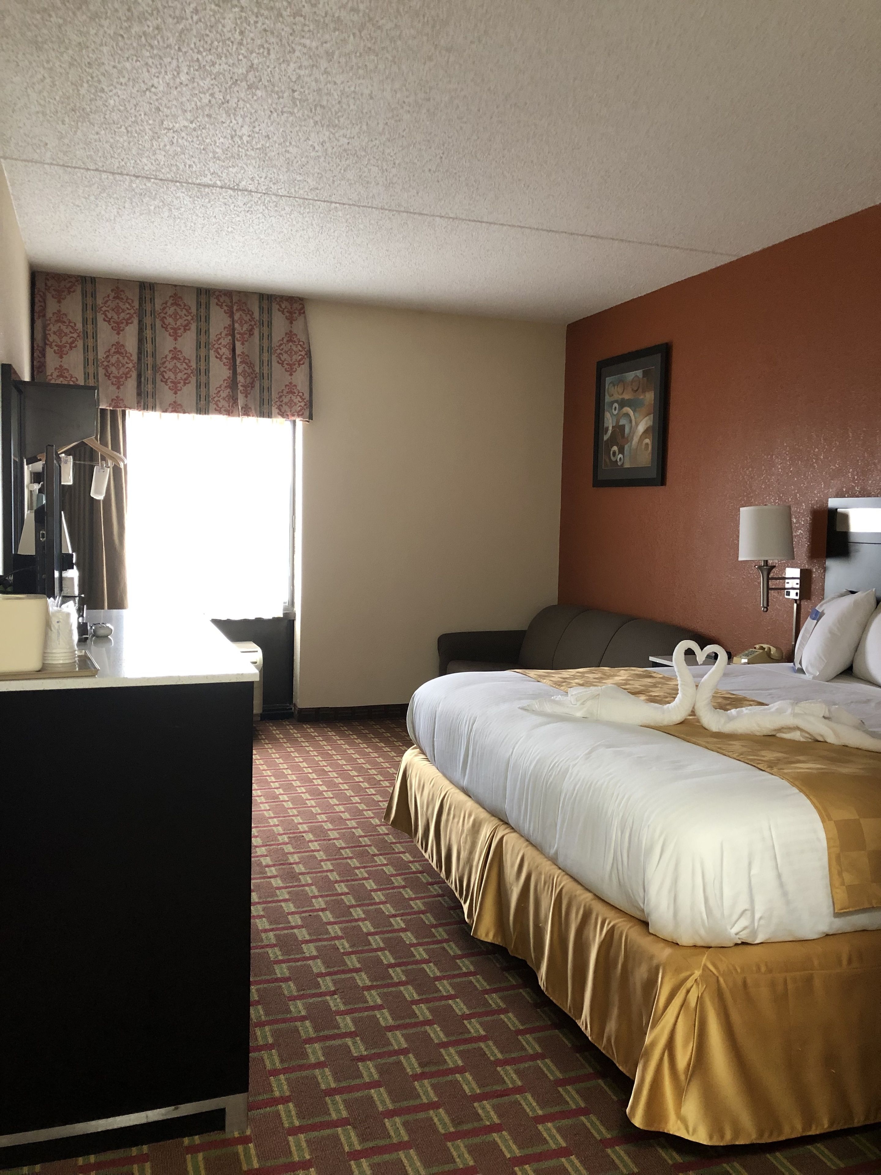 A hotel room with a bed, a desk, a chair, a lamp, and a painting on the wall.