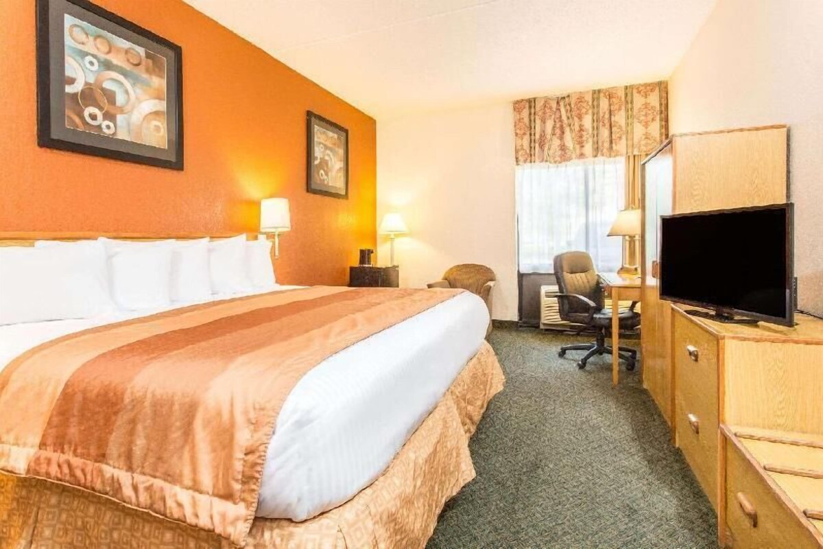 Une chambre d’hôtel équipée d’un lit, d’un bureau, d’une chaise, d’une télévision et décorée avec des œuvres d’art aux murs.