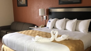A hotel room with a large bed, a desk, a chair, a lamp, and two framed artworks on the wall.