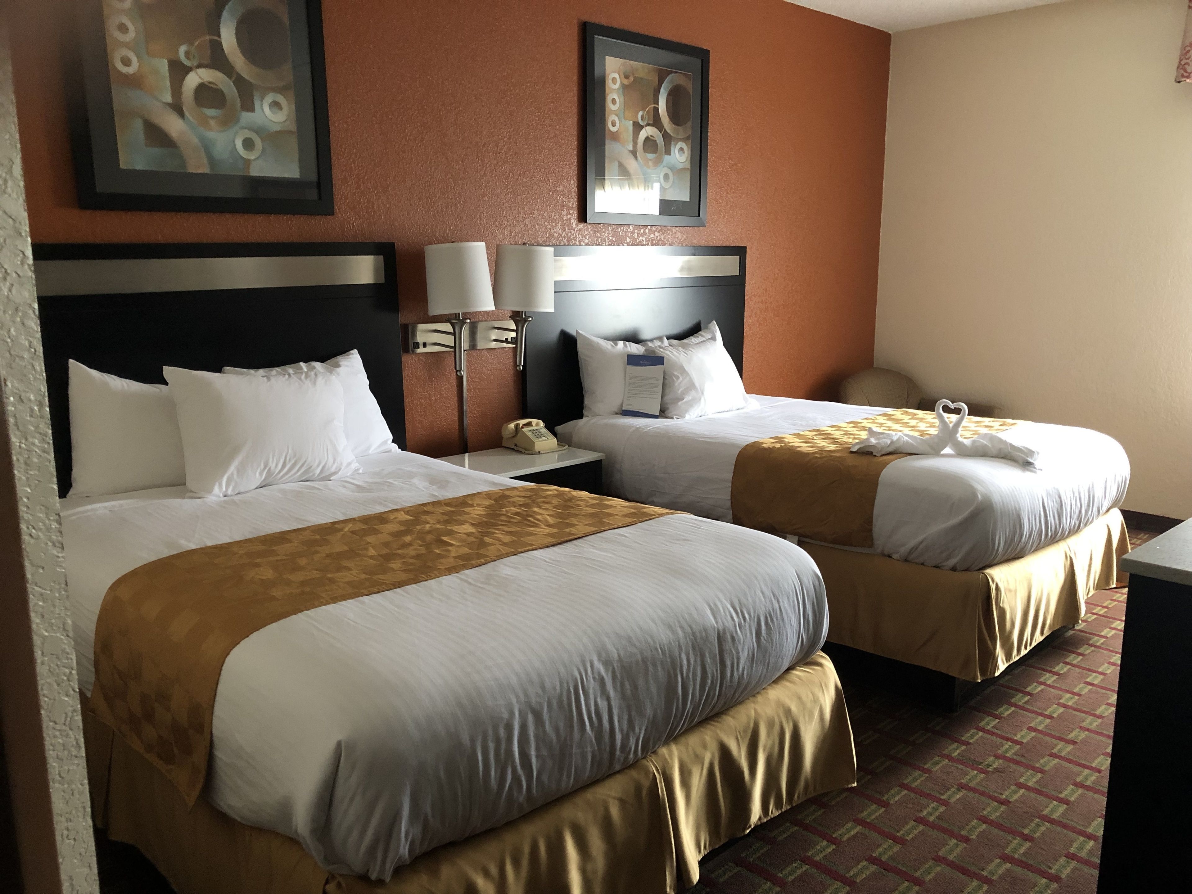 A hotel room with two beds, each with a headboard, white bedding, and a brown throw blanket. There are two bedside tables with lamps, a telephone, and a framed picture on the wall.