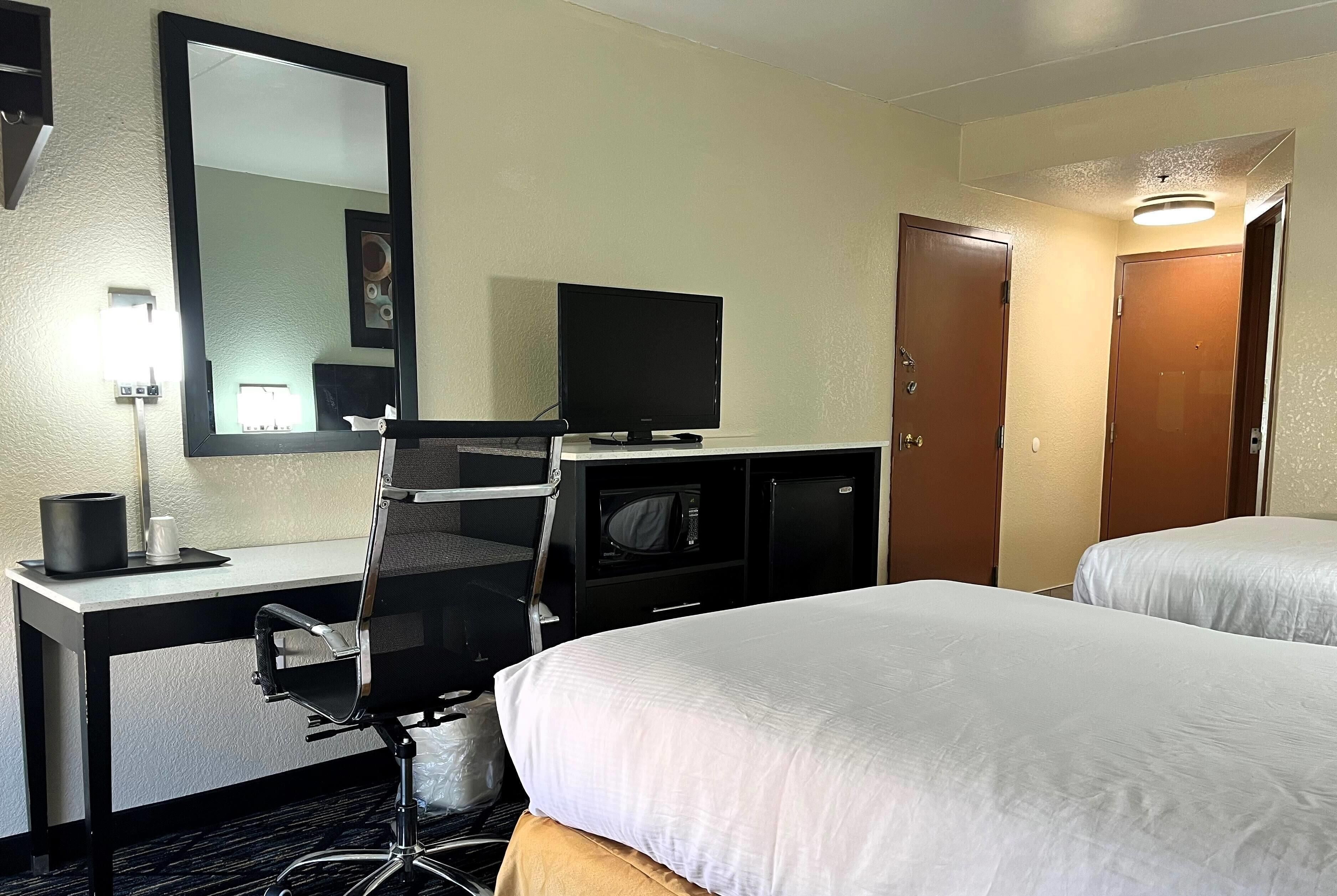 A hotel room with a desk, chair, television, two beds, and a mirror.