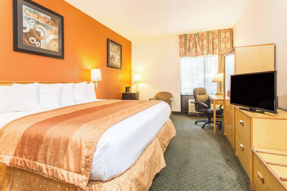 A hotel room with a large bed, a desk with a television, and a chair.