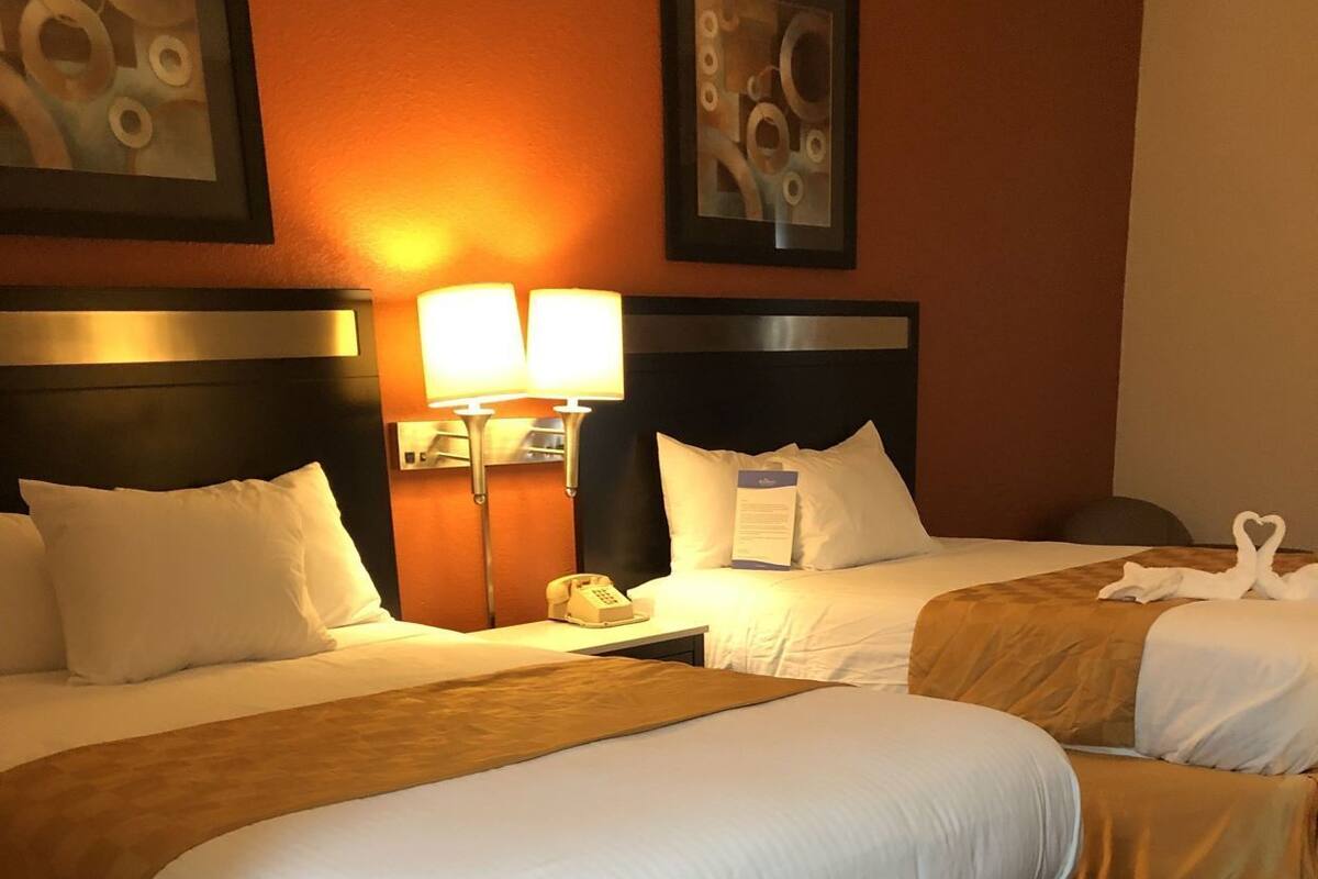 A hotel room with two beds, a nightstand, a lamp, and a telephone.
