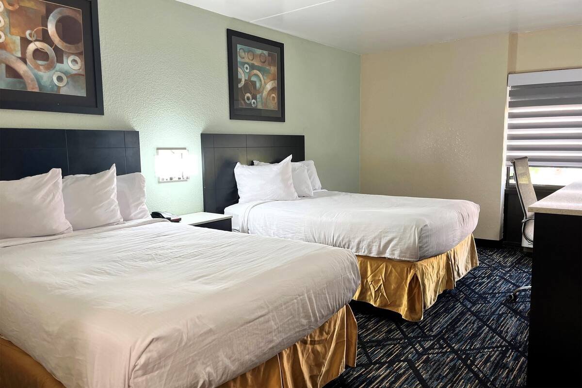 A hotel room with two beds, a desk, and a window with blinds.