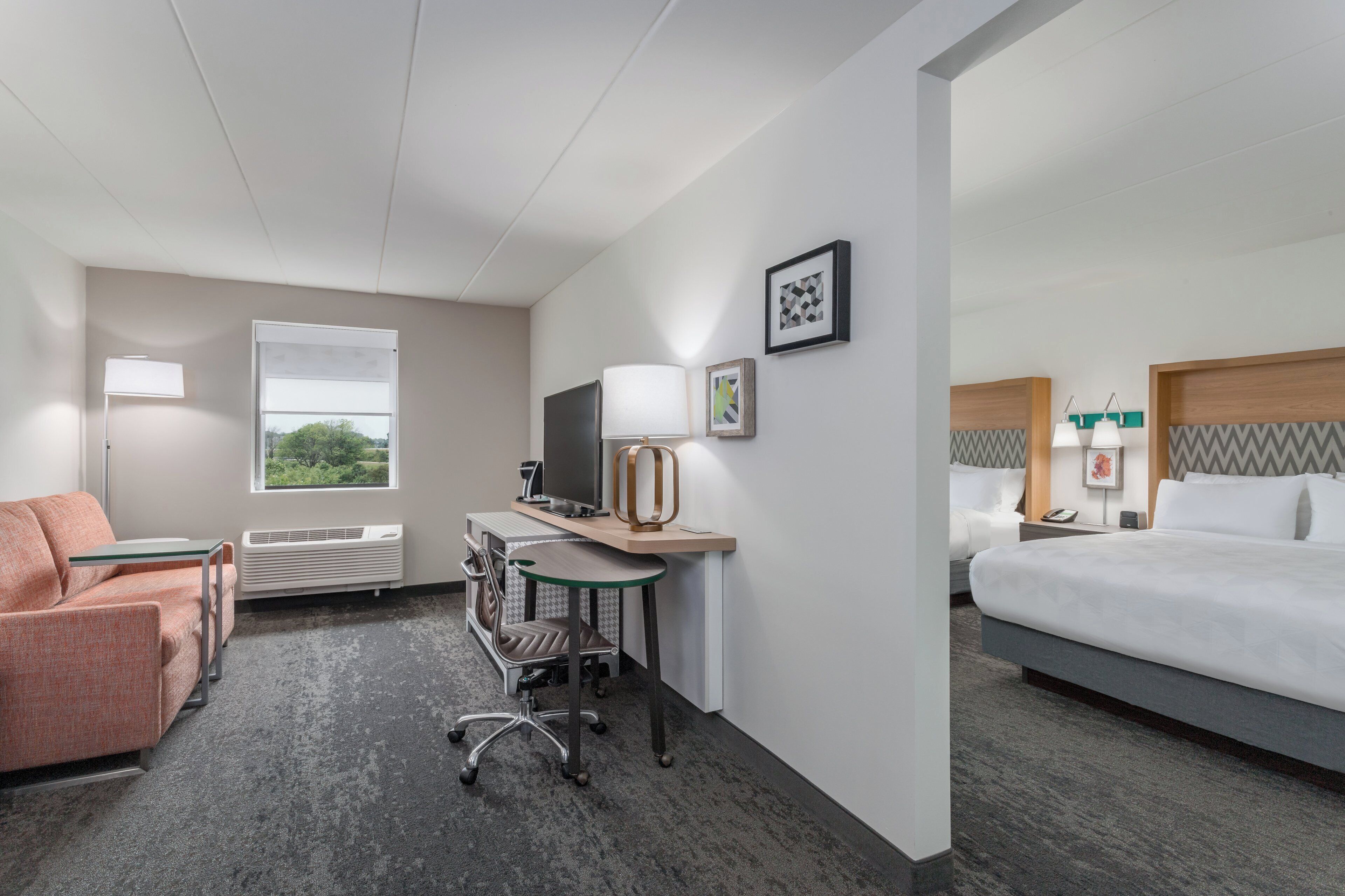 A hotel room with a bed, a desk with a computer, a chair, a sofa, and a window.