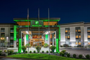 A Holiday Inn hotel with a modern facade, green accent lighting, and a flagpole.