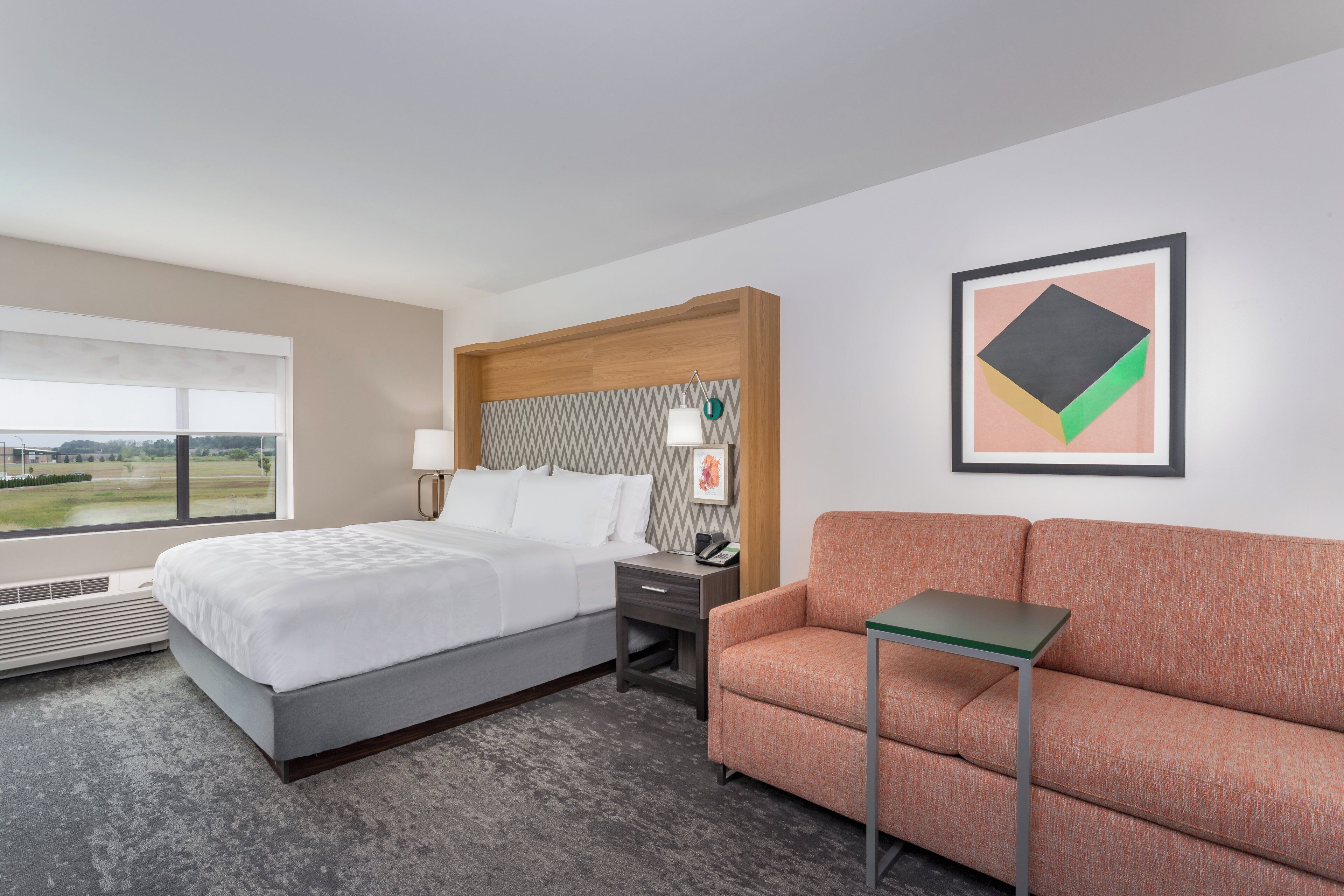 A hotel room with a bed, a desk, a chair, a small table, and a window with a view.