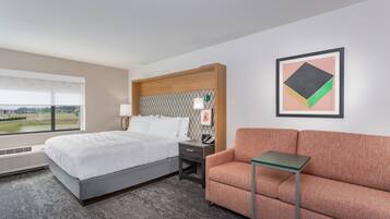 A hotel room with a bed, a desk, a chair, a small table, and a window with a view.