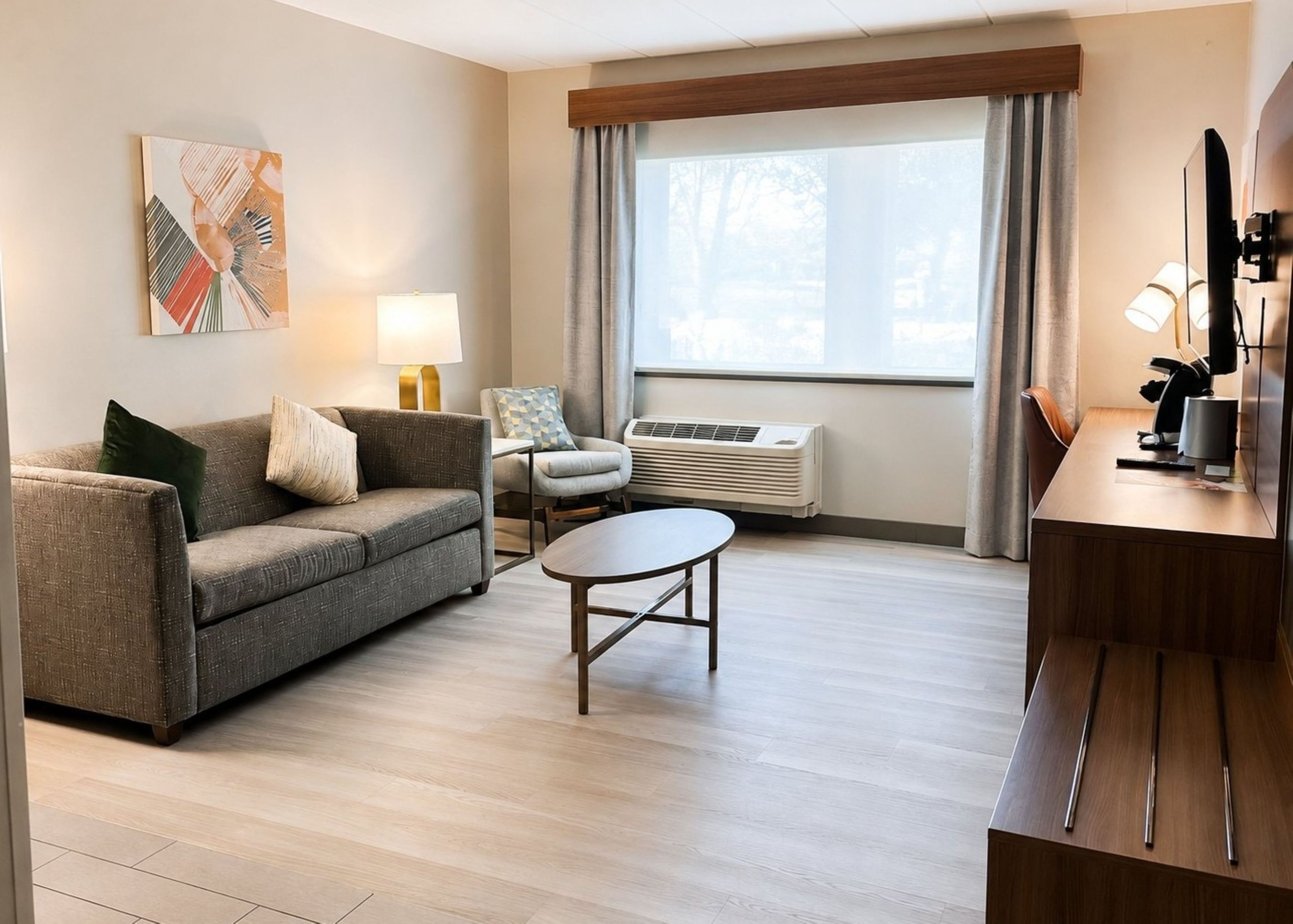 A modern living room with a sofa, a coffee table, a chair, a lamp, an air conditioning unit, and a window with curtains.