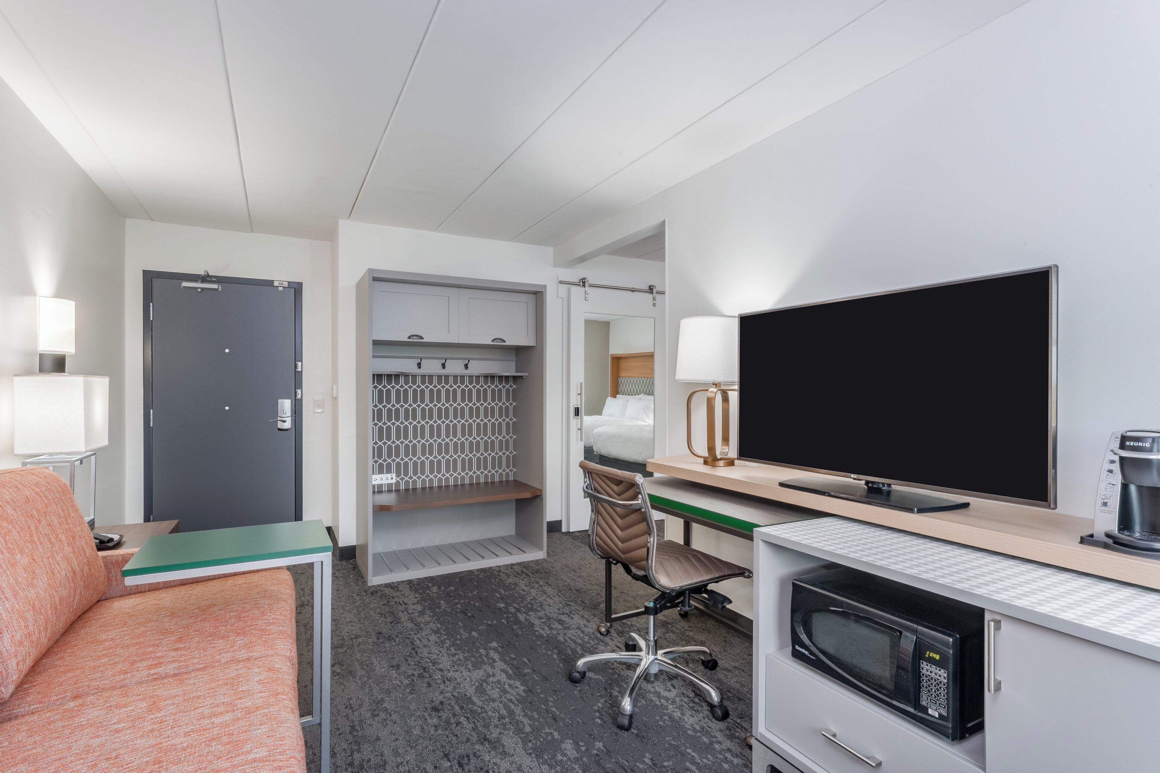 A hotel room with a bed, a desk with a computer, a television, a microwave, and a minibar.