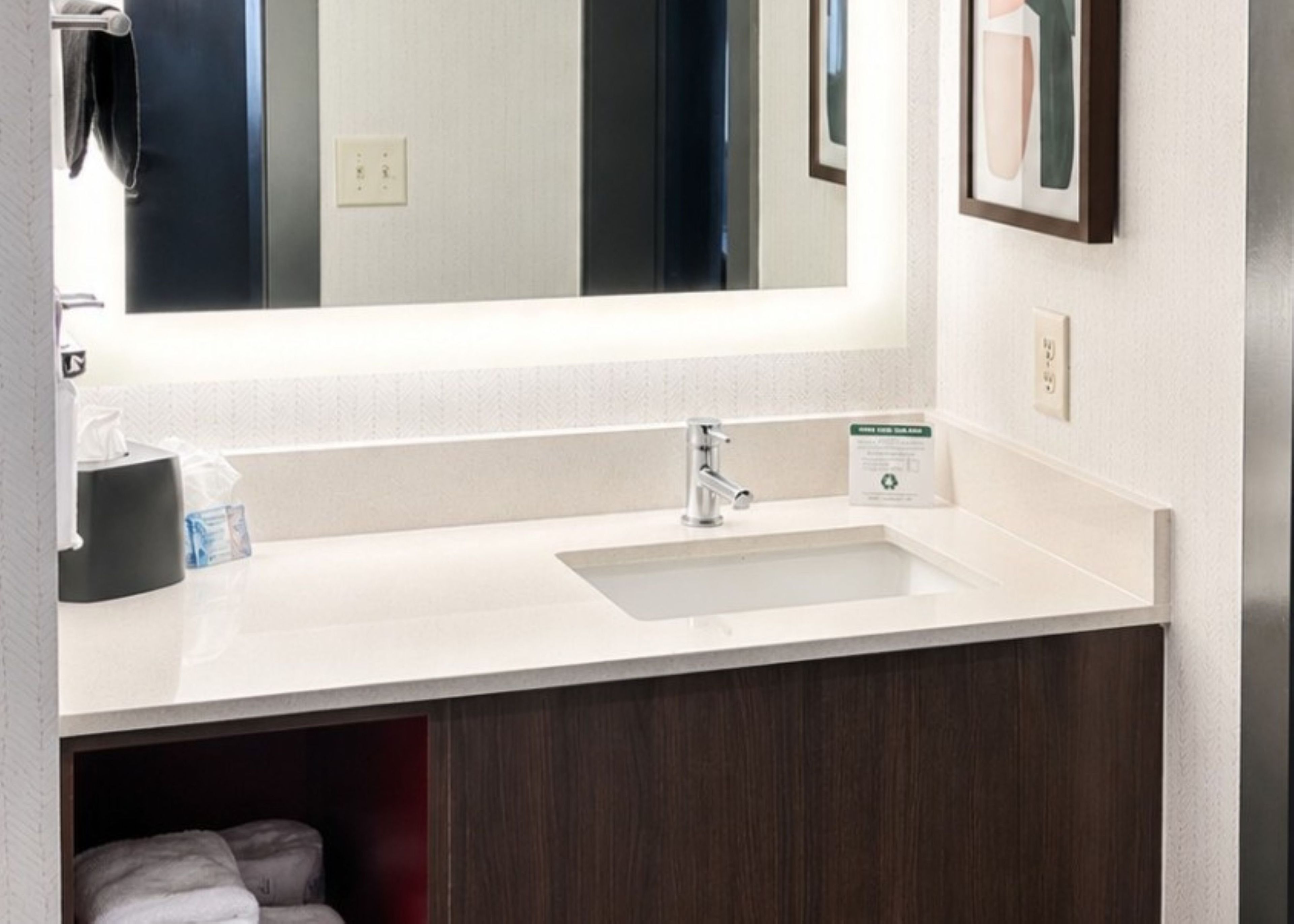 A hotel bathroom with a white sink, a mirror, and a towel rack.
