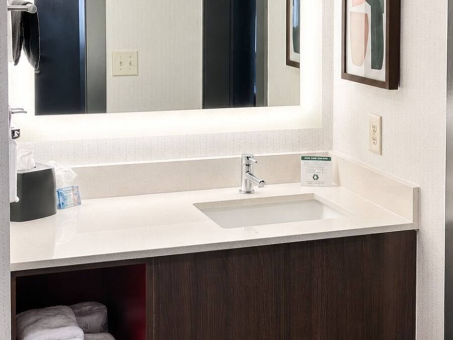 A hotel bathroom with a white sink, a mirror, and a towel rack.